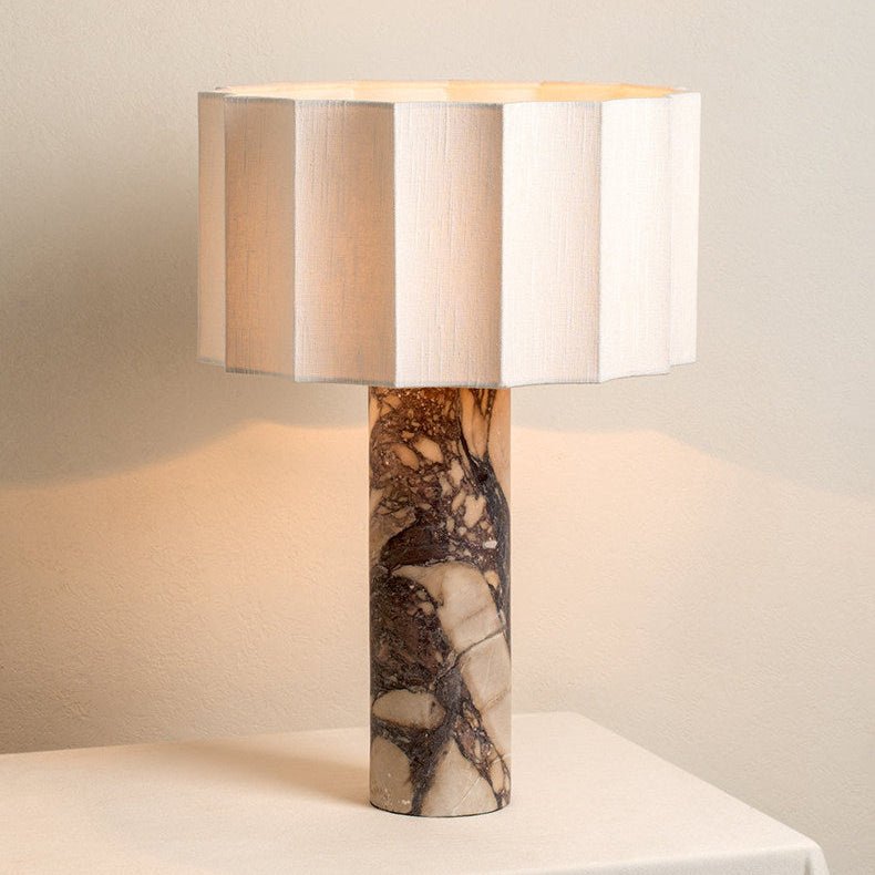 The Clérachic table lamp glows warm from another angle, its faceted shade lit above the tall purple marble base.