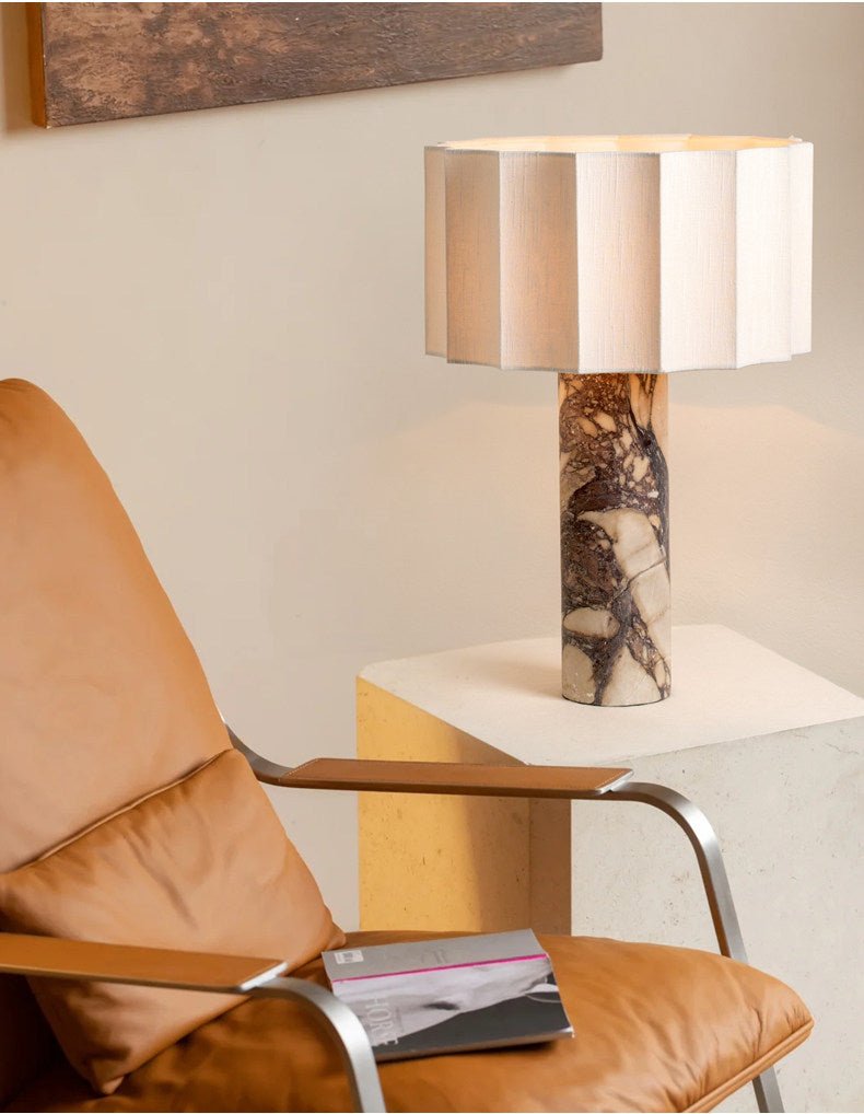 The Clérachic table lamp on its stone plinth beside a tan leather armchair with a magazine left open on the seat.