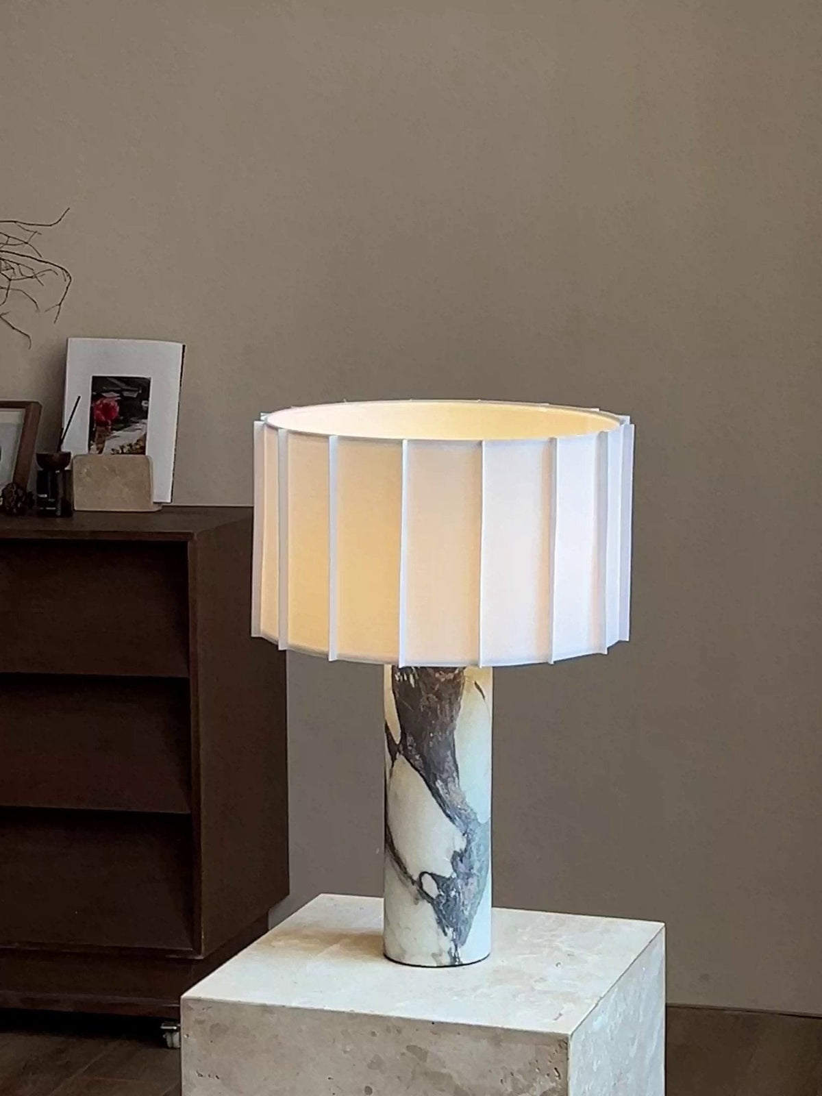 The Clérachic table lamp stands on a stone plinth beside a low wooden chest topped with a framed photograph.
