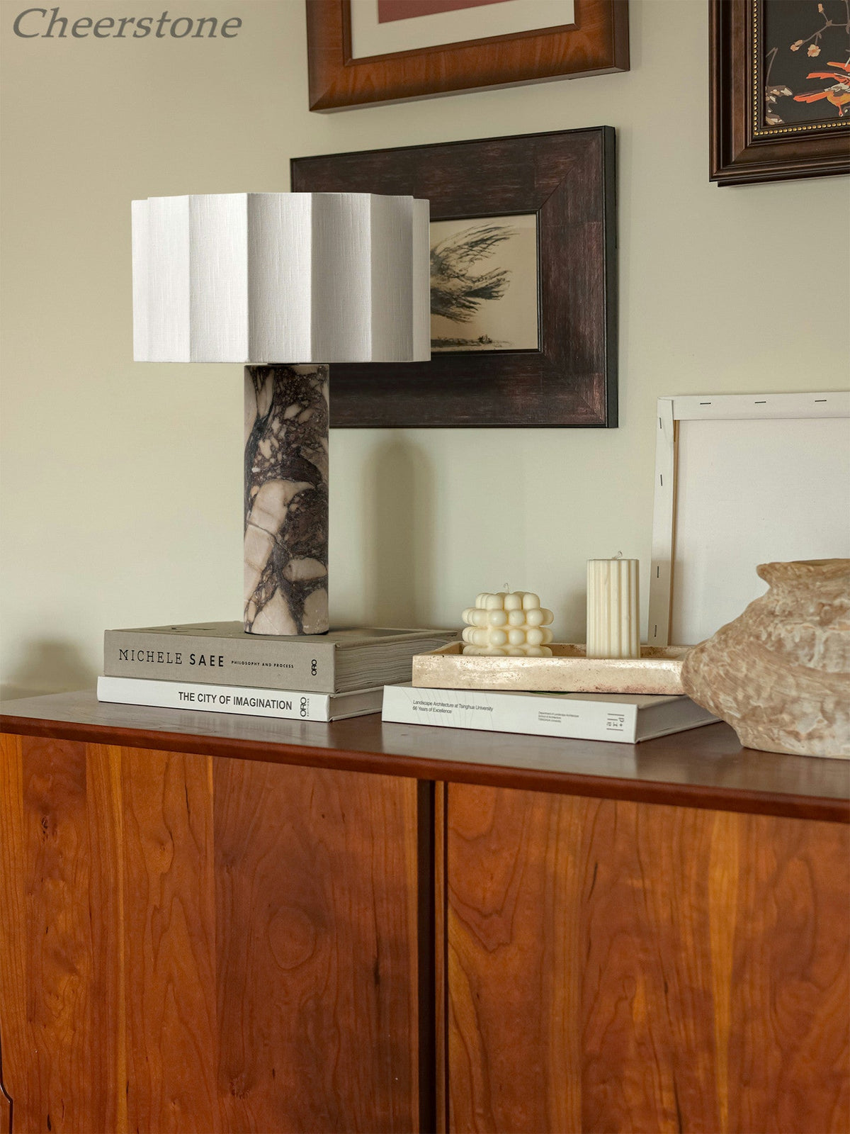 The Clérachic table lamp sits on a wooden sideboard beneath framed art, styled among stacked books and a small vase.
