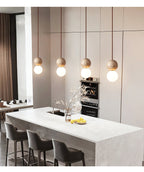 A row of Clérachic pendants lines a kitchen island with white marble countertop and dark panelled cabinetry.