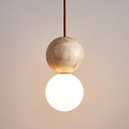 A travertine sphere rests above its lit opal glass globe on this Clérachic pendant, seen close up.