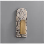 Clérachic marble arch wall sconce photographed unlit on a plain grey studio wall, showing the arched stone shape and brass panel.