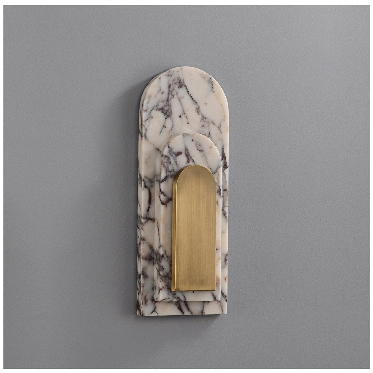 Clérachic marble arch wall sconce photographed unlit on a plain grey studio wall, showing the arched stone shape and brass panel.