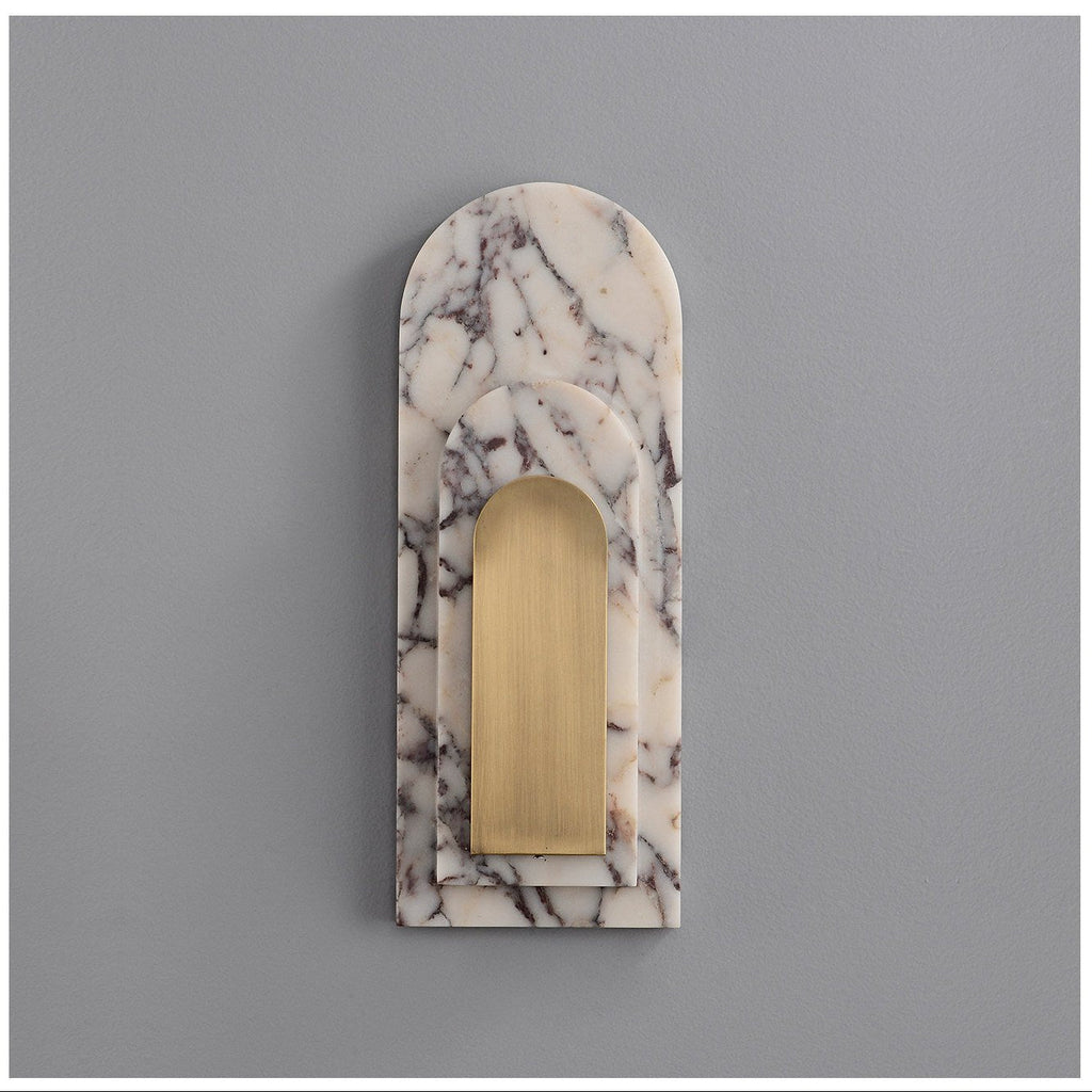 Another studio view of the unlit Clérachic marble sconce, showing the veining across the arched stone face and brass inset up close.