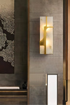 Aurevon sconce glowing on a stone-clad wall in a hotel-style entrance beside a dark artwork