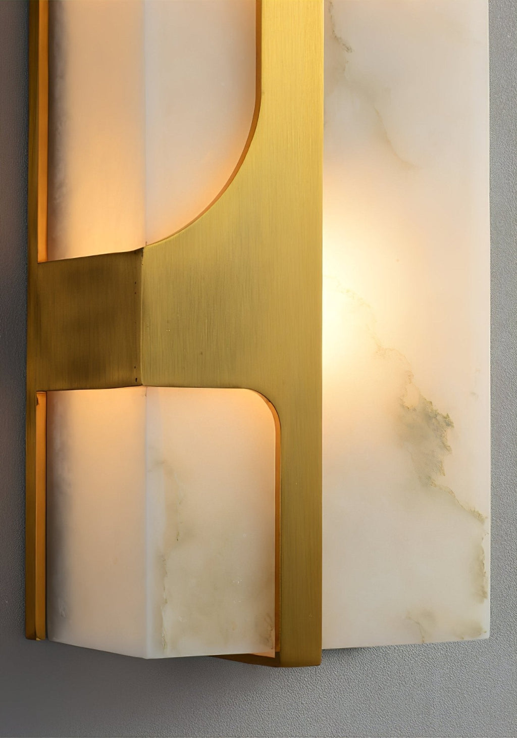 Close-up of the Aurevon sconce brushed brass bracket where it crosses the backlit alabaster panel