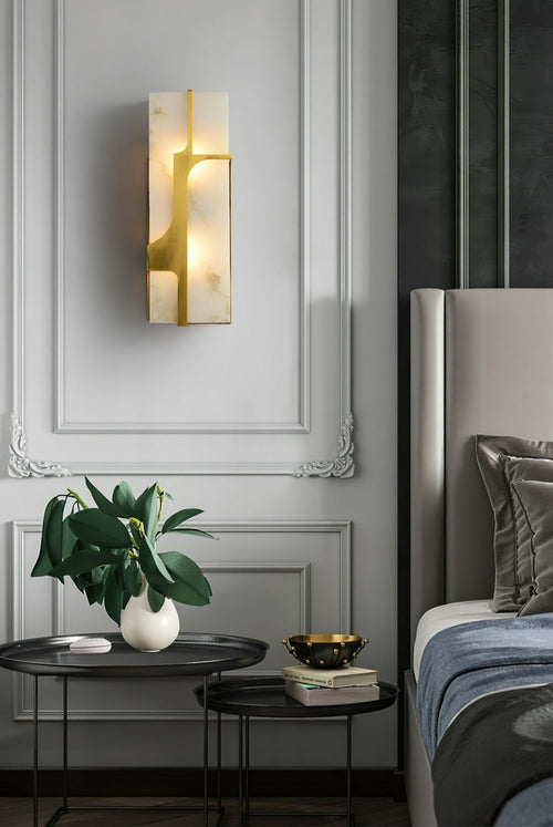 Aurevon sconce on a moulded bedroom wall above black nesting tables beside an upholstered bed