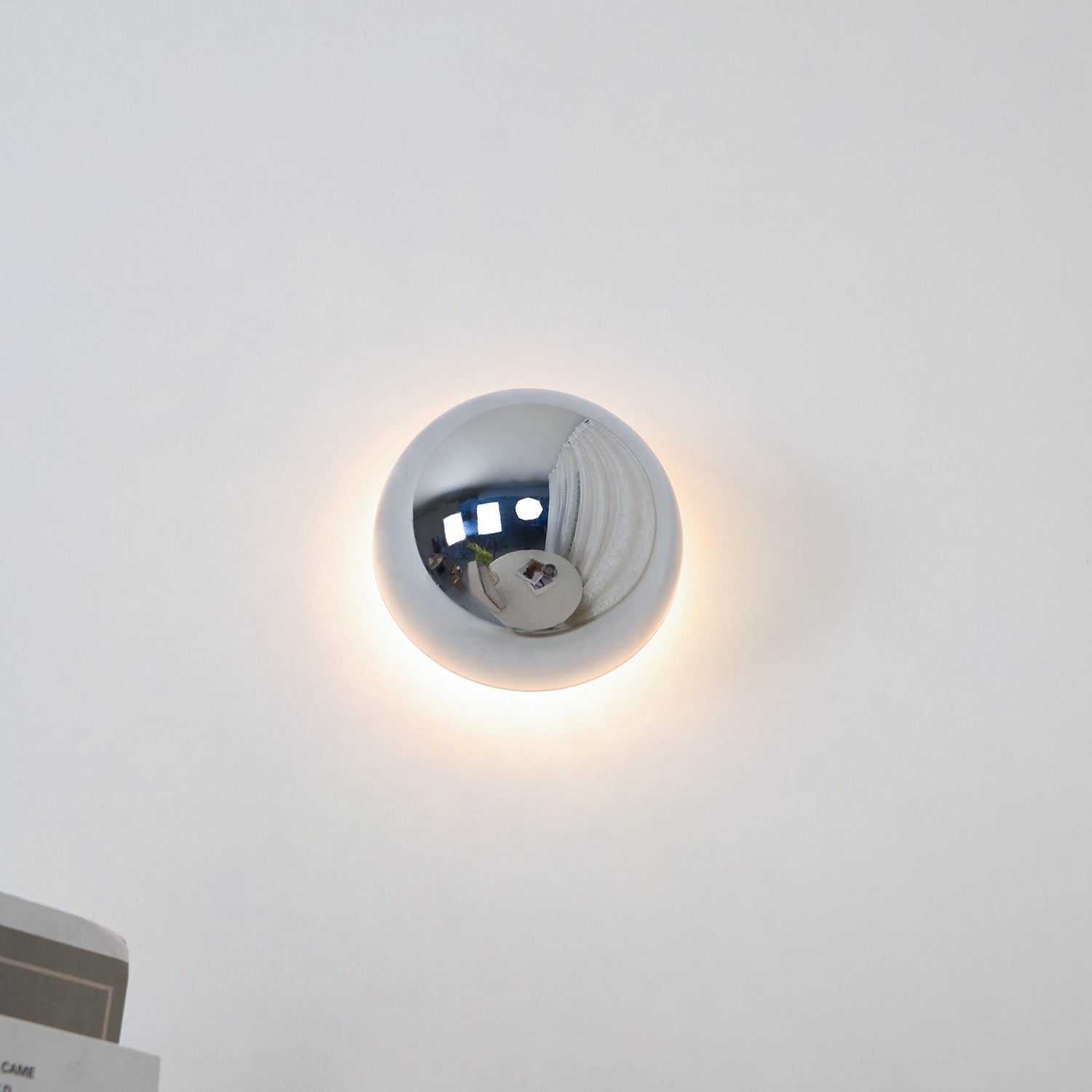 Polished sphere wall sconce with warm light on a wall