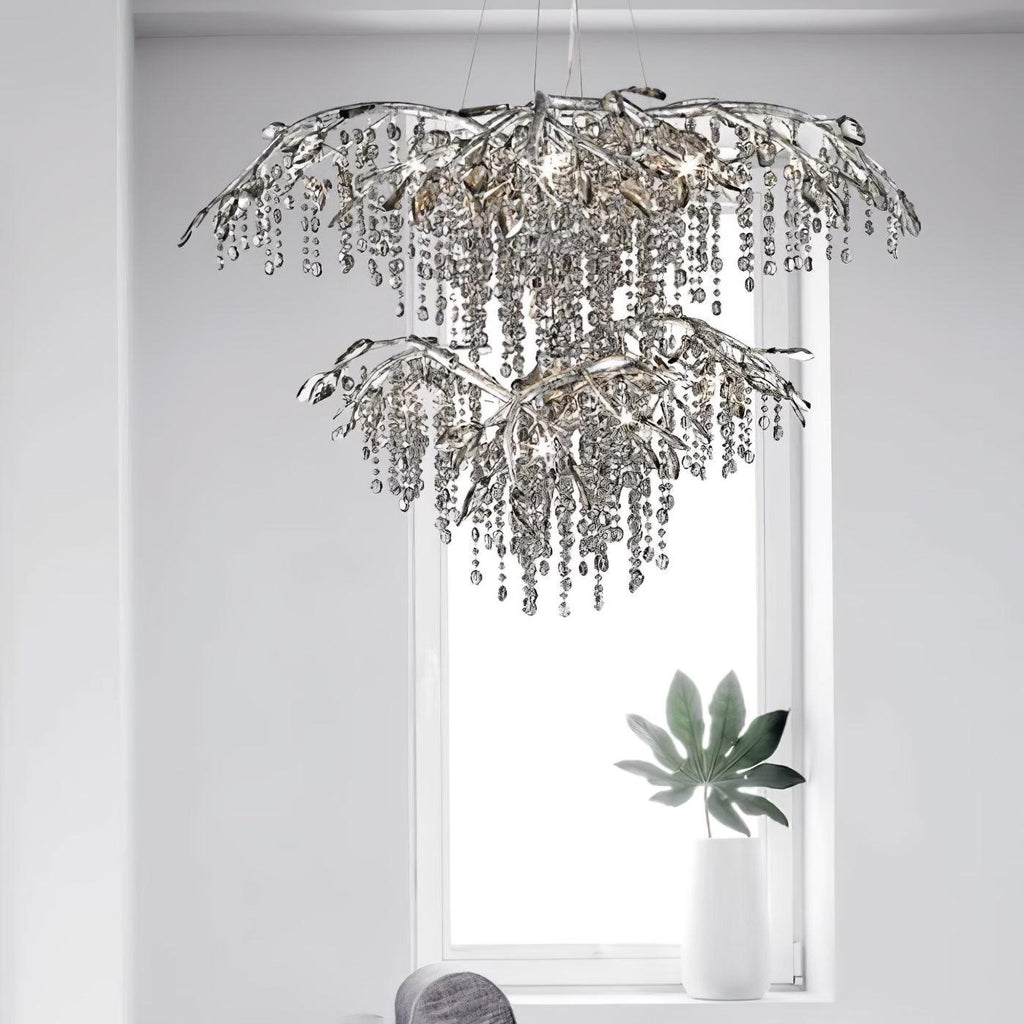The two-tier silver chandelier hung in front of a bright window, a leafy plant below.
