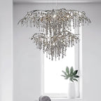 The two-tier silver chandelier hung in front of a bright window, a leafy plant below.