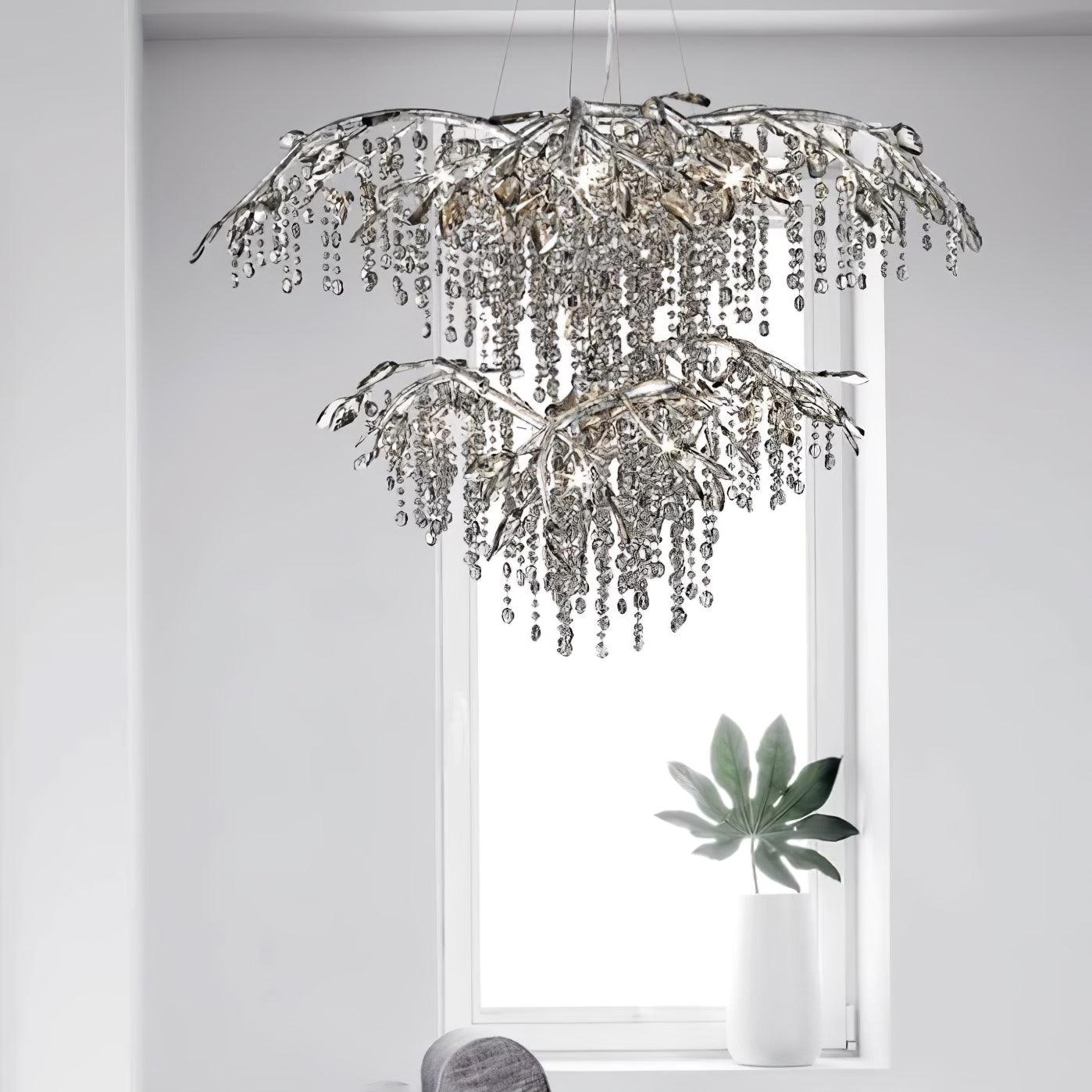 The two-tier silver chandelier hung in front of a bright window, a leafy plant below.