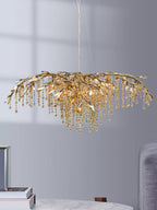 The gold chandelier lit in a grey room above a marble table stacked with books.