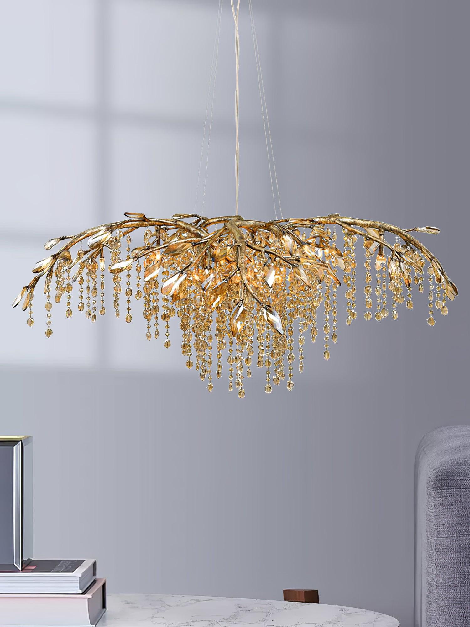 The gold chandelier lit in a grey room above a marble table stacked with books.