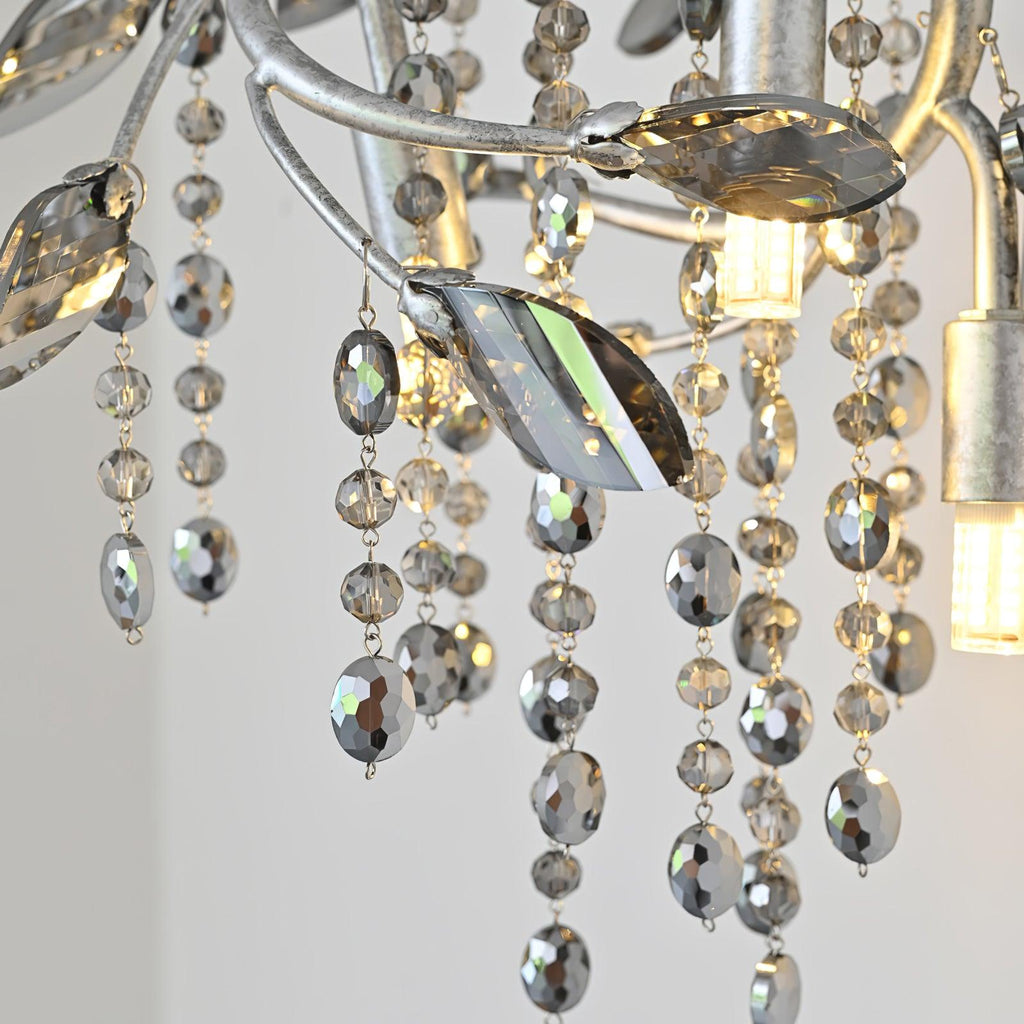 Close-up of the leaf-shaped crystals and faceted bead strands, with a bulb lit behind.