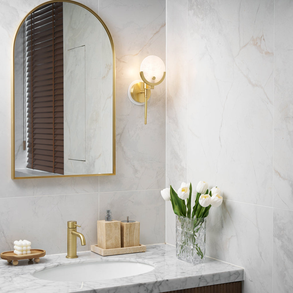 Clérachic wider bathroom view with the Zavarara sconce lit above a marble counter, brass tap and basin below.