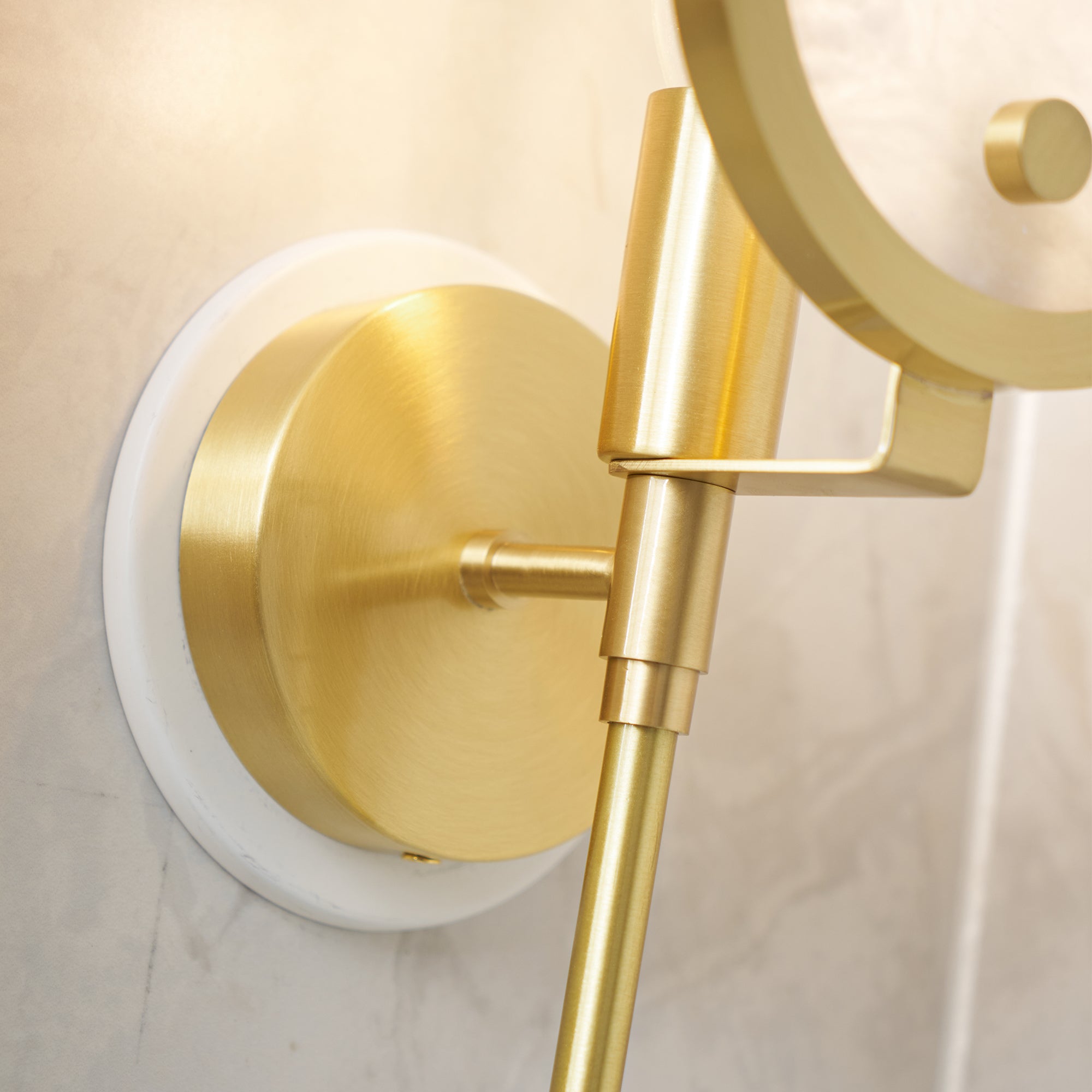 Clérachic close detail of the brass backplate and its white stone ring against a marble wall, warmly lit.