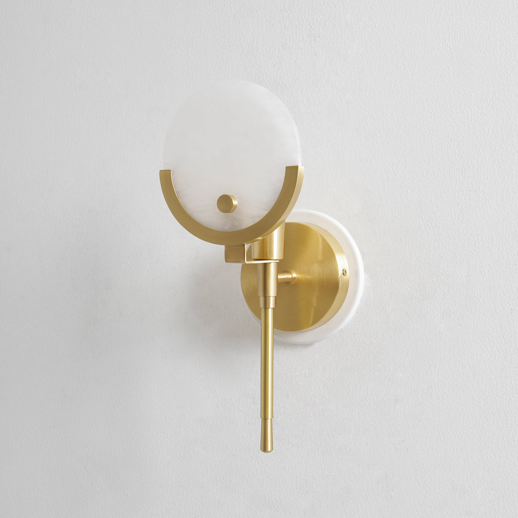 Clérachic zavarara wall light seen at an angle, its alabaster sphere shade cradled in a brushed brass half-ring.