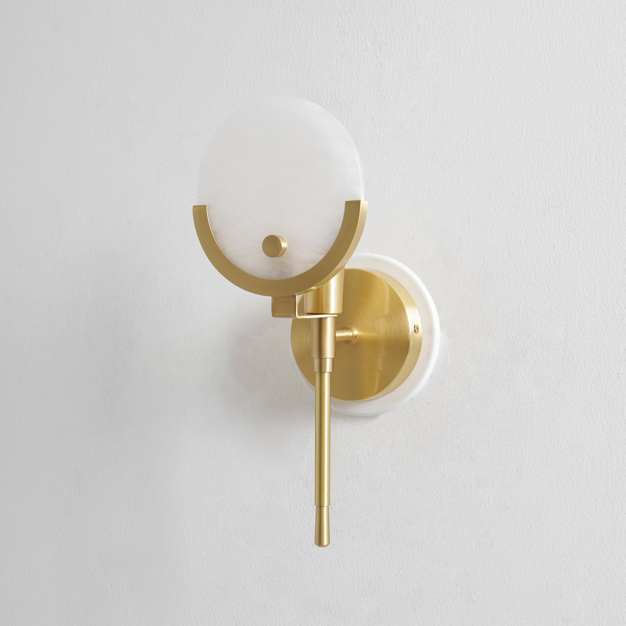 Clérachic zavarara wall light seen at an angle, its alabaster sphere shade cradled in a brushed brass half-ring.