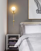 Clérachic zavarara wall light lit beside a bed, glowing softly above a nightstand stacked with books.