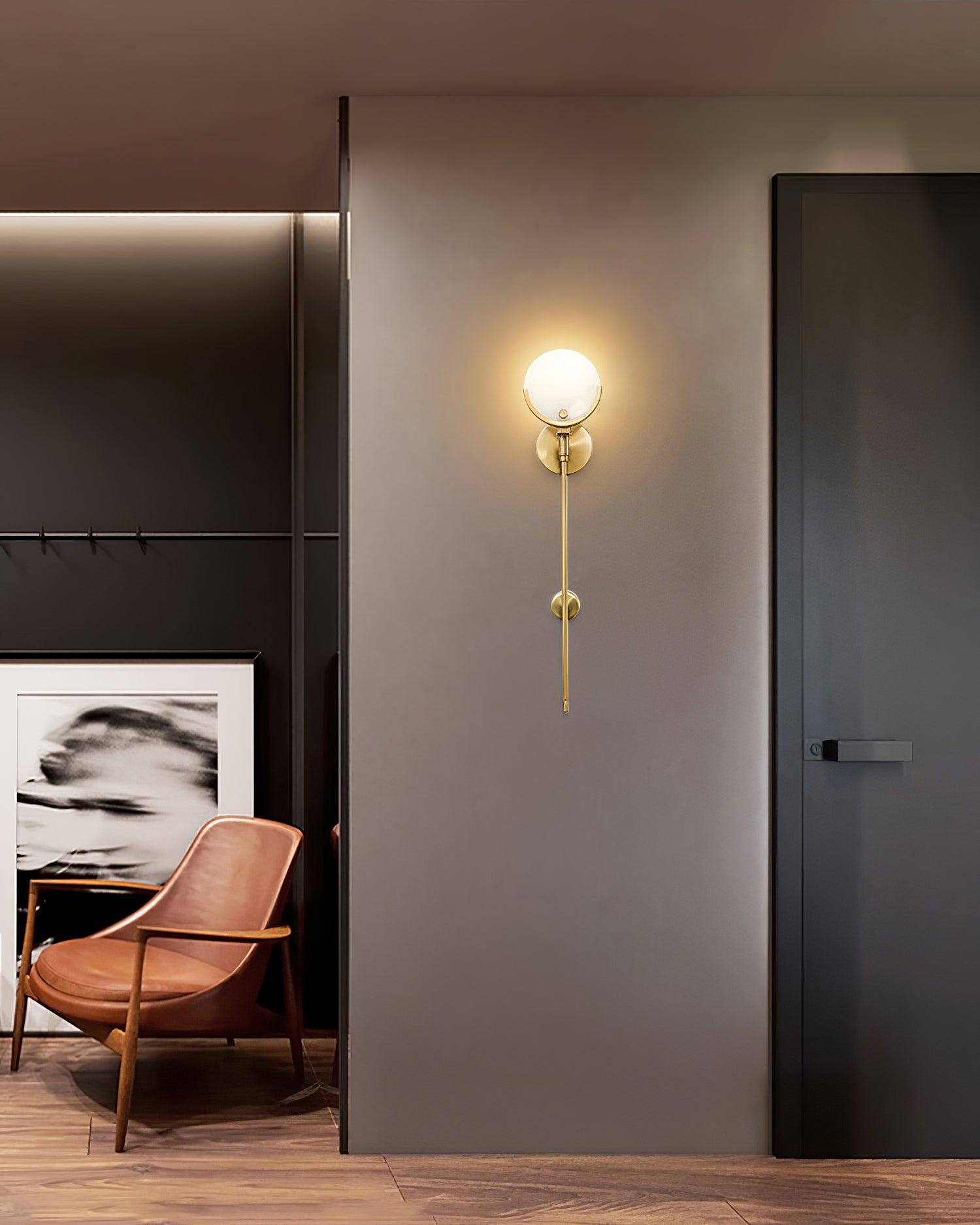 Clérachic zavarara sconce lit on a grey hallway wall, with a tan leather chair and dark door alongside.
