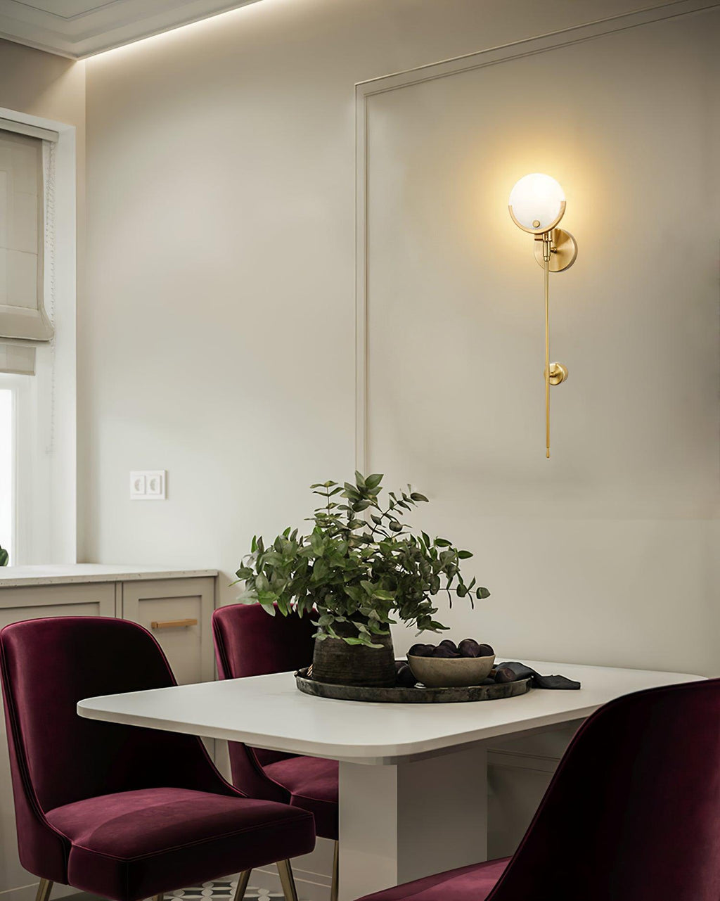 Clérachic zavarara wall light glowing above a dining nook set with a white table and burgundy velvet chairs.