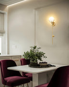 Clérachic zavarara wall light glowing above a dining nook set with a white table and burgundy velvet chairs.