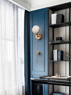 Clérachic zavarara wall light unlit on a deep blue panelled wall in a study, beside a black bookshelf.