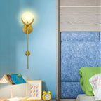 Clérachic tall sconce lit on the blue wall of a child's room above picture frames and a yellow alarm clock.