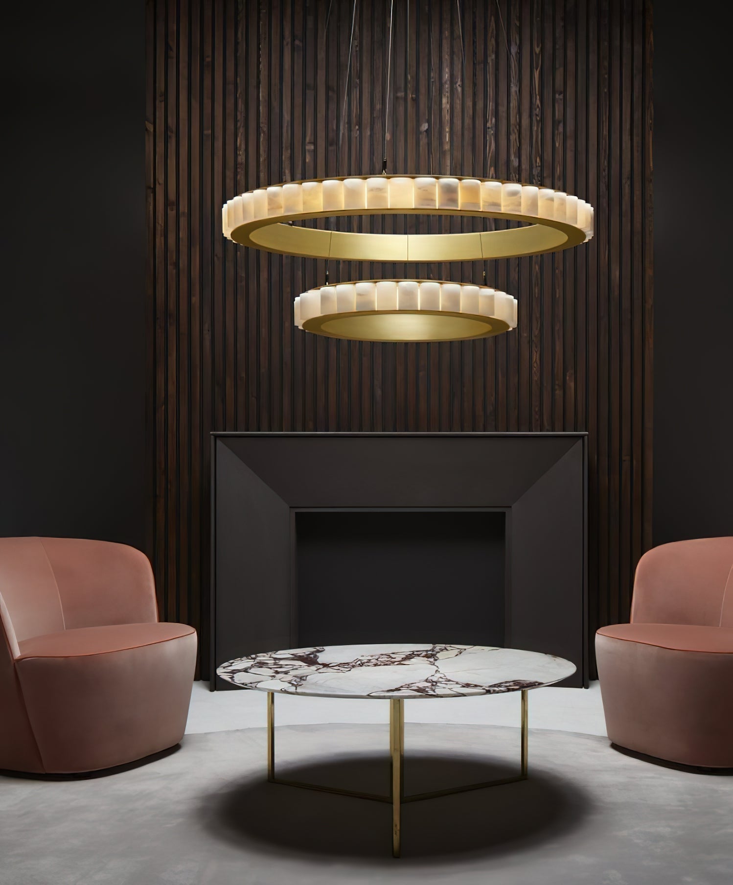 Two-tier brass alabaster chandelier lit above a black fireplace flanked by pink velvet armchairs.