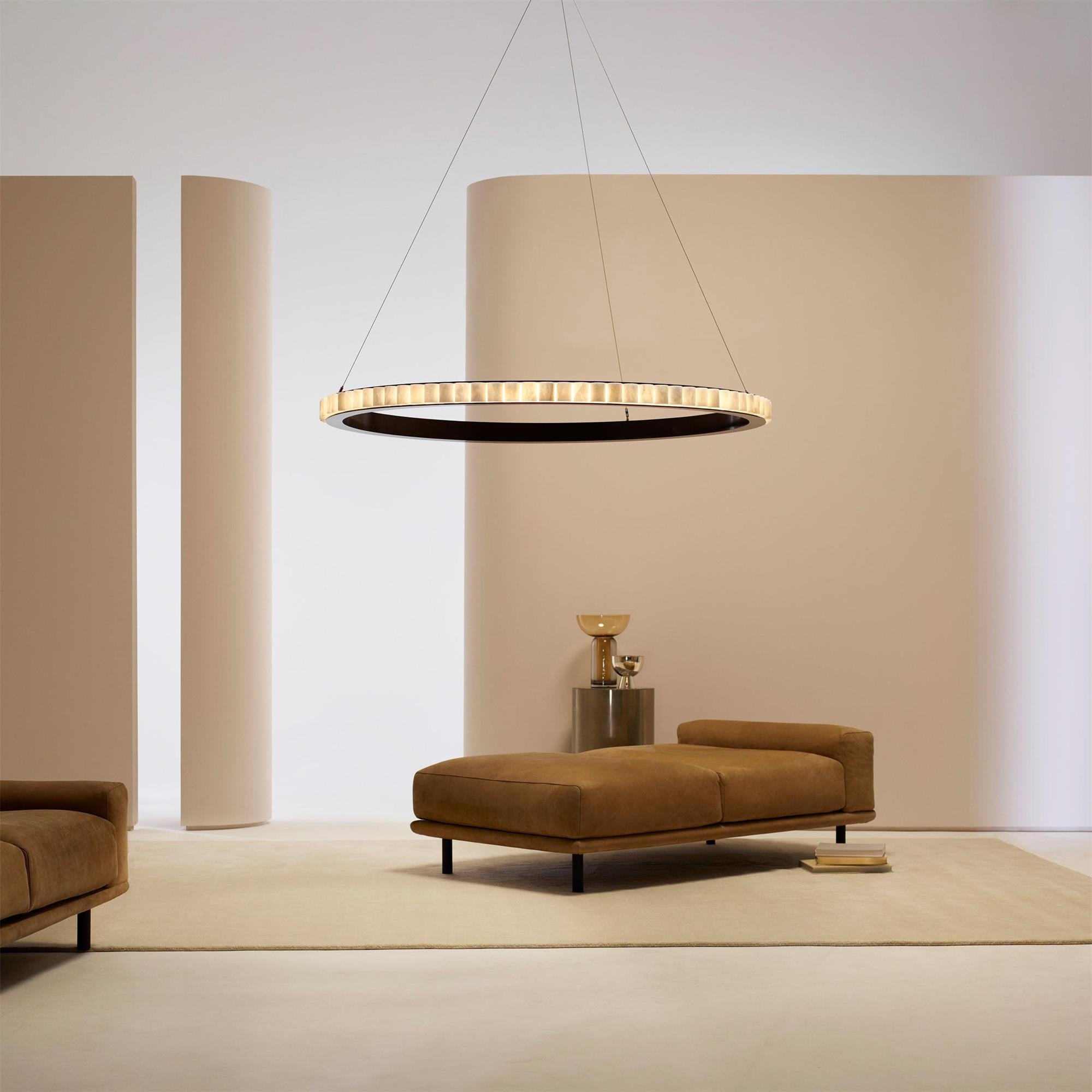 Large alabaster chandelier lit above a tan leather daybed in a room of curved beige walls.