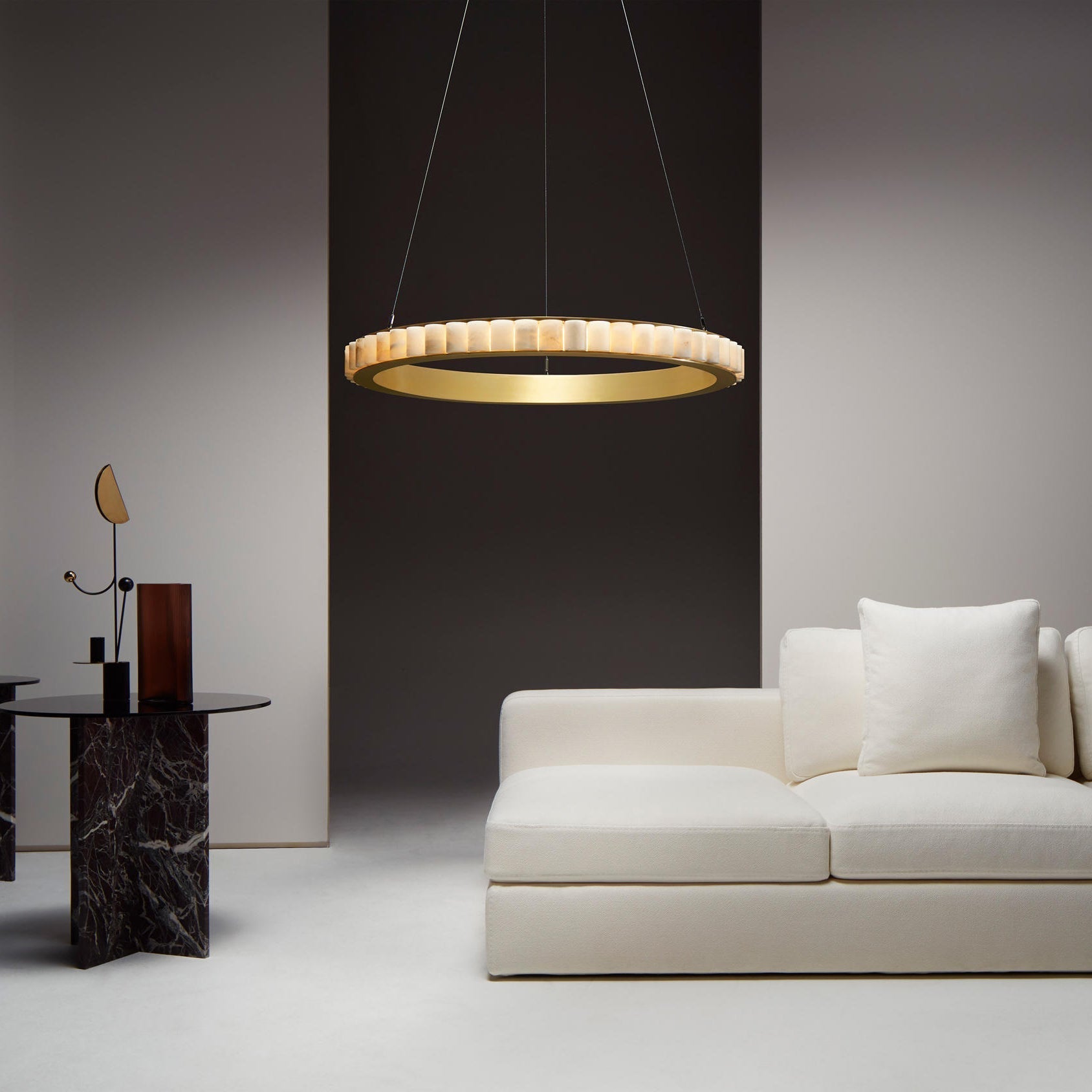 Brass alabaster chandelier lit above a white sofa in a living room with a dark brown wall.