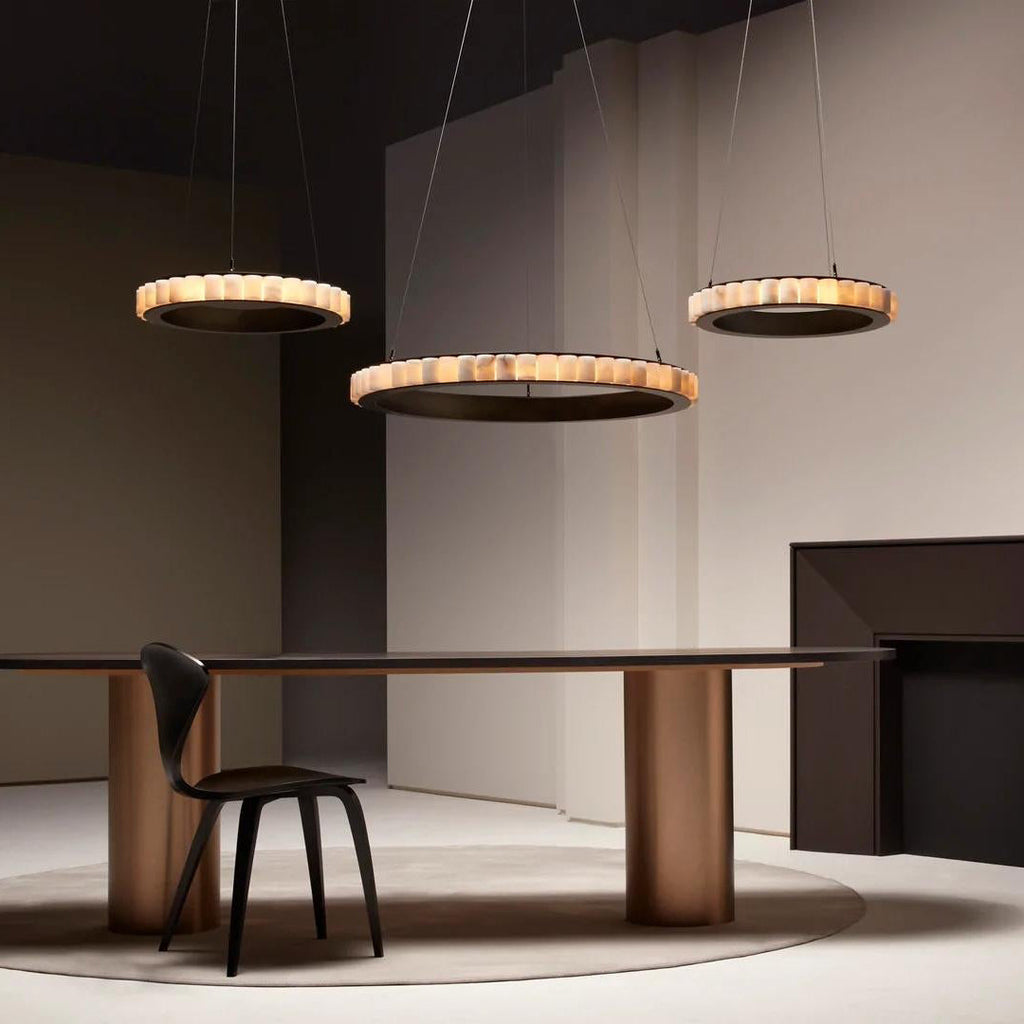 Three dark bronze alabaster chandeliers lit at staggered heights above a long dining table.