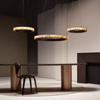 Three dark bronze alabaster chandeliers lit at staggered heights above a long dining table.