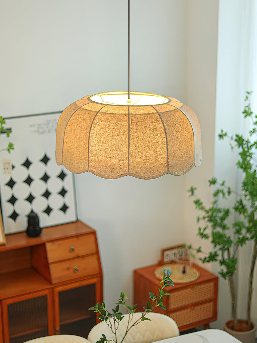Beside a curtained window with a houseplant and patterned wall art, this beige Clérachic pendant lamp glows softly.