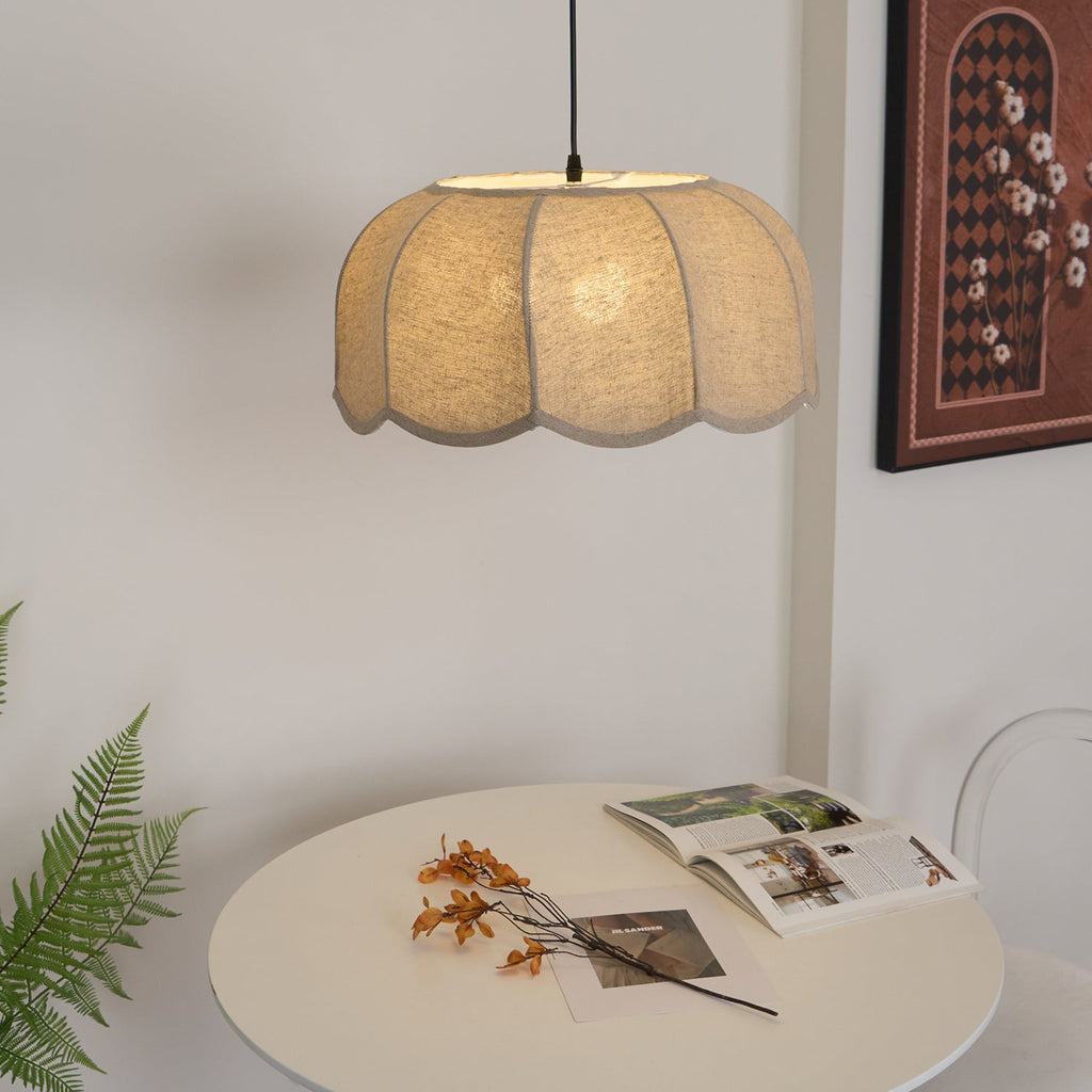 Seen from underneath, this beige Clérachic pendant lamp hangs above a round table with a fern sprig and a magazine.