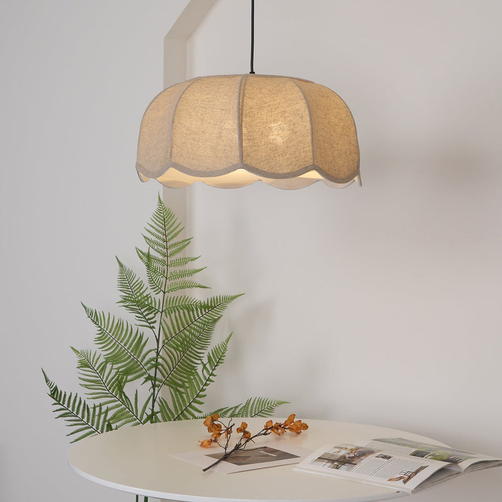 A round white table styled with a fern frond and an open magazine sits beneath this lit beige Clérachic pendant lamp.