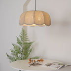 A round white table styled with a fern frond and an open magazine sits beneath this lit beige Clérachic pendant lamp.