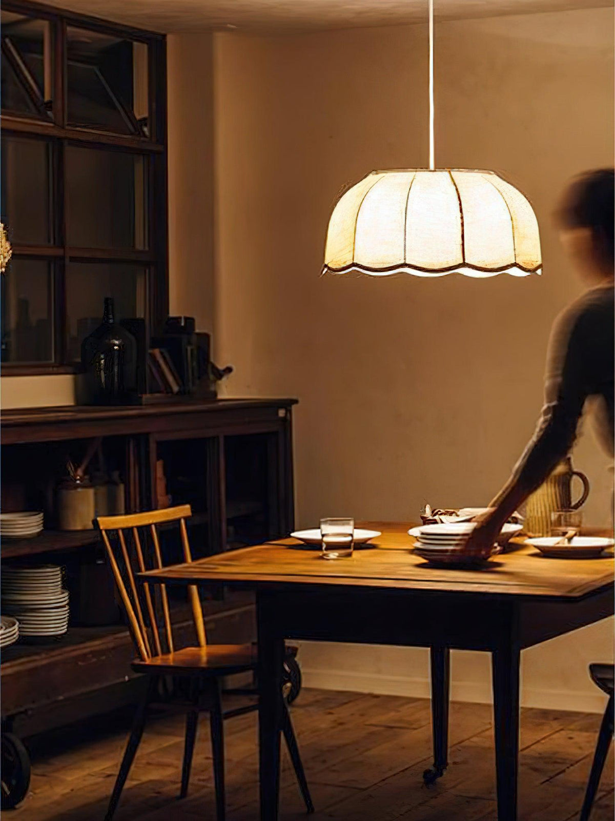 Someone sets out plates in a rustic kitchen beneath this lit beige Clérachic pendant lamp.