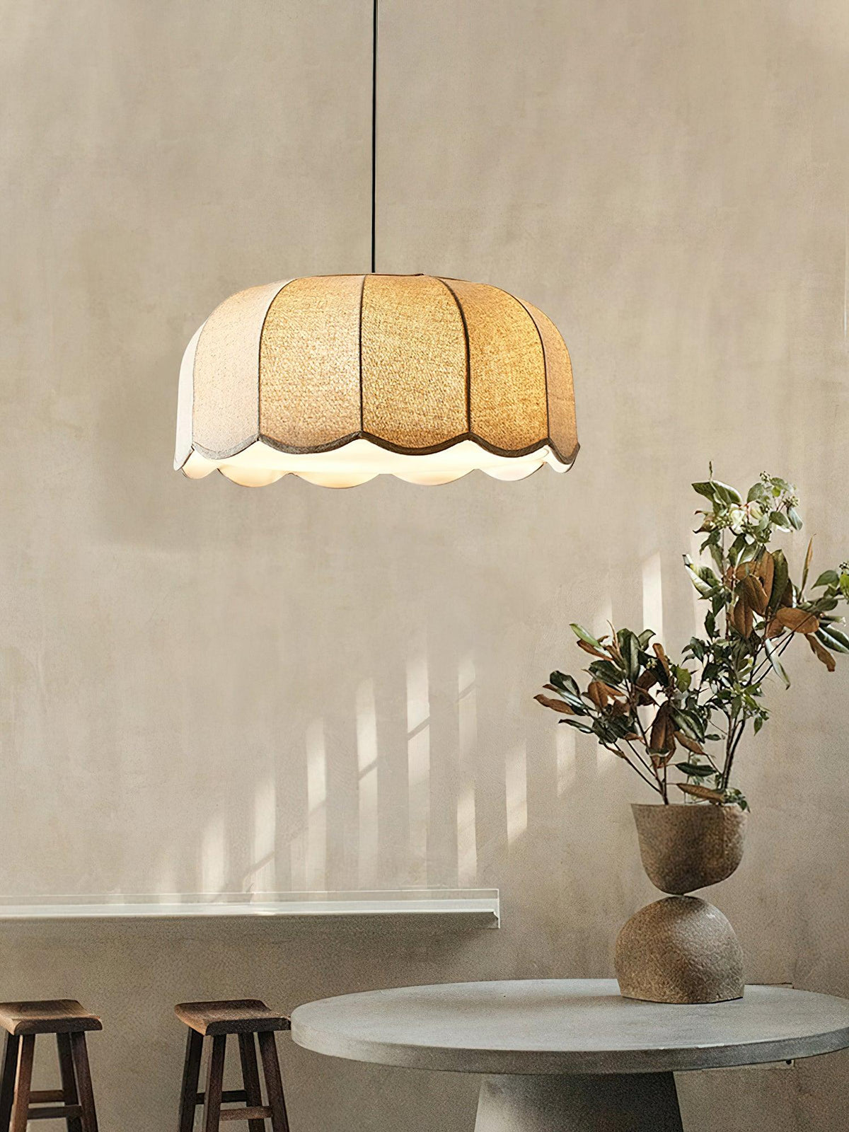 Above a round stone table with a magnolia branch, this beige Clérachic pendant lamp glows on a warm textured wall.