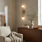 This Clérachic sconce in brass finish hangs above a walnut sideboard, a cream armchair with a throw beside it.