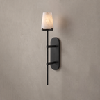 In matte black, this Clérachic wall sconce glows against a plain warm-grey wall, its tapered alabaster shade lit.