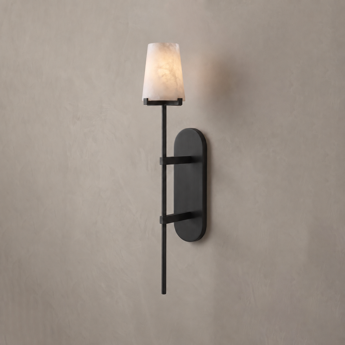 In matte black, this Clérachic wall sconce glows against a plain warm-grey wall, its tapered alabaster shade lit.