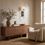 A black Clérachic sconce lights an entry wall above a walnut sideboard dressed with olive branches and a ceramic vase.