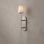 A brushed-nickel Clérachic wall sconce stands unlit against a plain grey wall, its tapered alabaster shade catching the light.