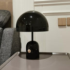 In black, this Clérachic table lamp rests on a grey tray table near a sofa and a panelled white wall with light switches.