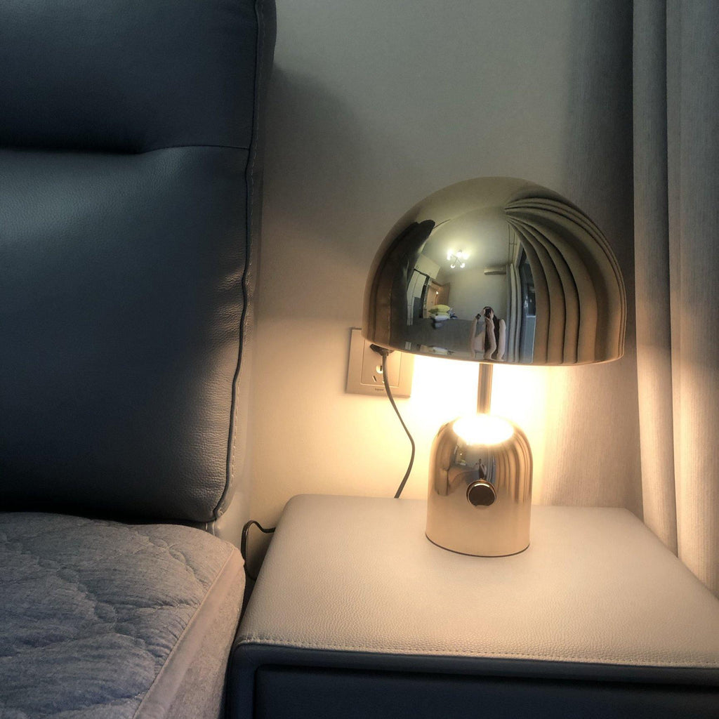 Lit warmly on a nightstand beside a dark leather headboard, this Clérachic chrome table lamp casts a soft glow.