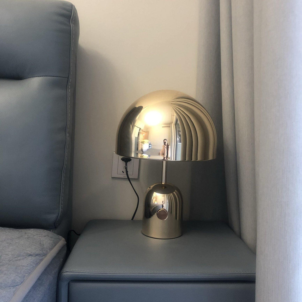 This Clérachic table lamp in a brass finish glows on a grey tufted nightstand beside a matching headboard.