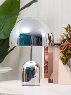 A tall chrome dome lamp and a shorter matching one from Clérachic stand on a marble surface beside pink flowers.