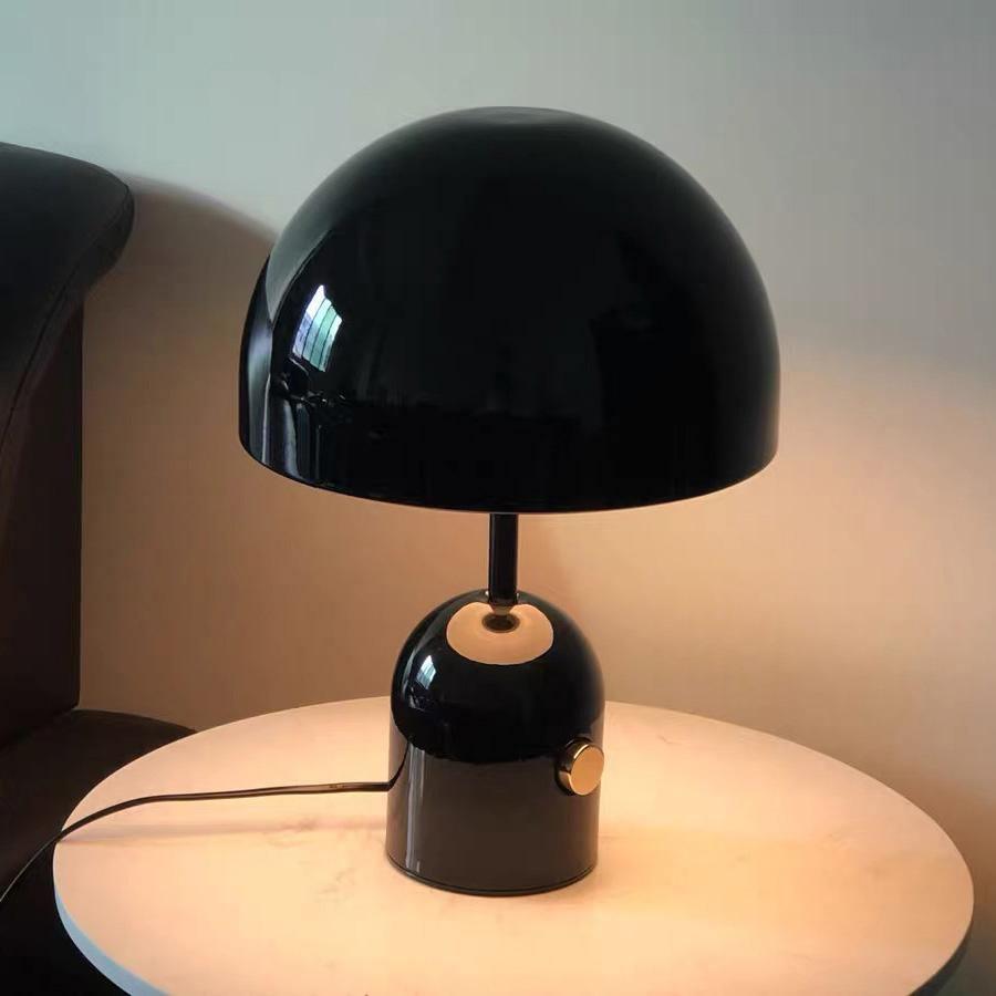 This Clérachic black table lamp stands on a round white surface, its cord visible, with a dark leather chair behind.